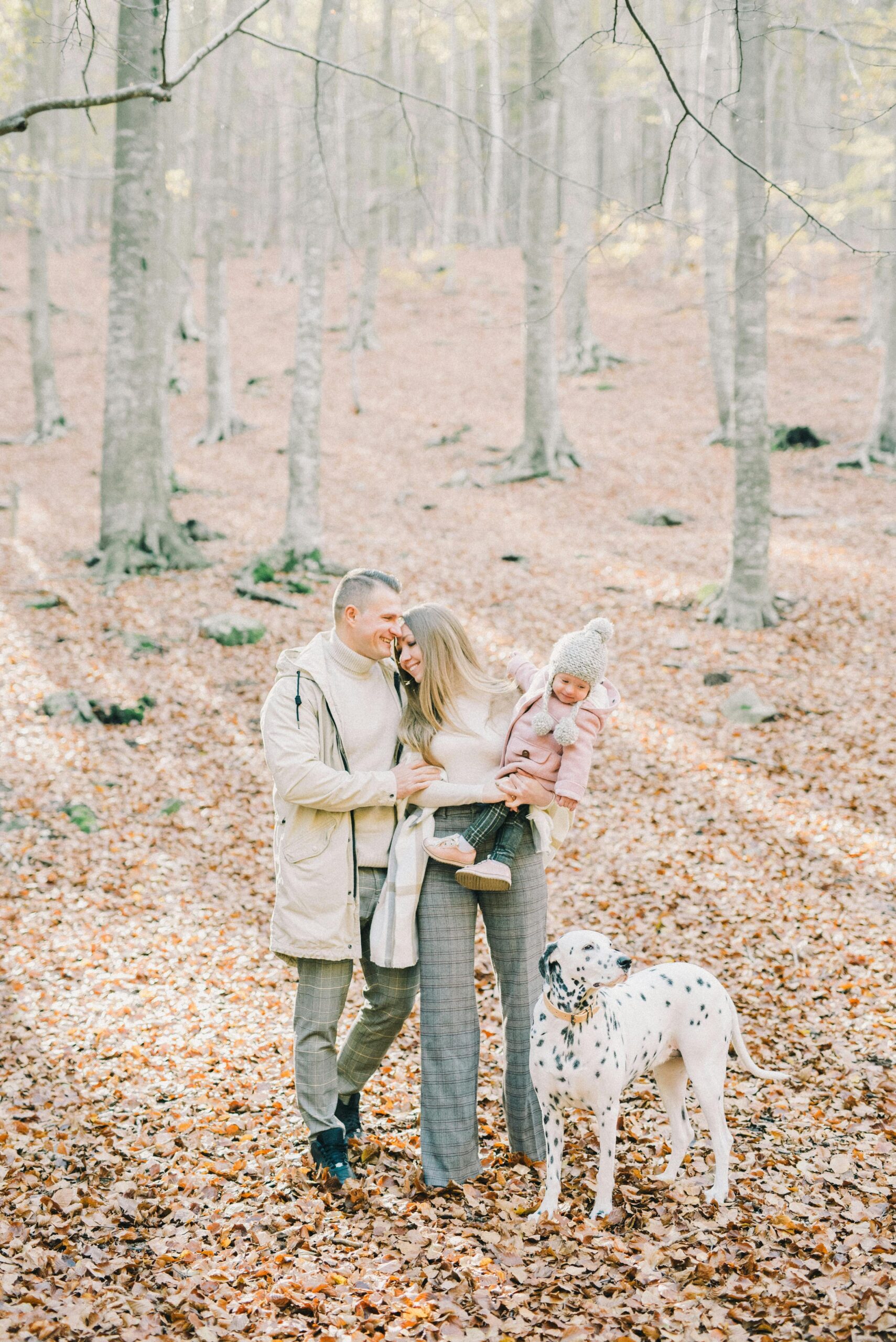 Family with a dog walking through fallen leaves in neutral layers