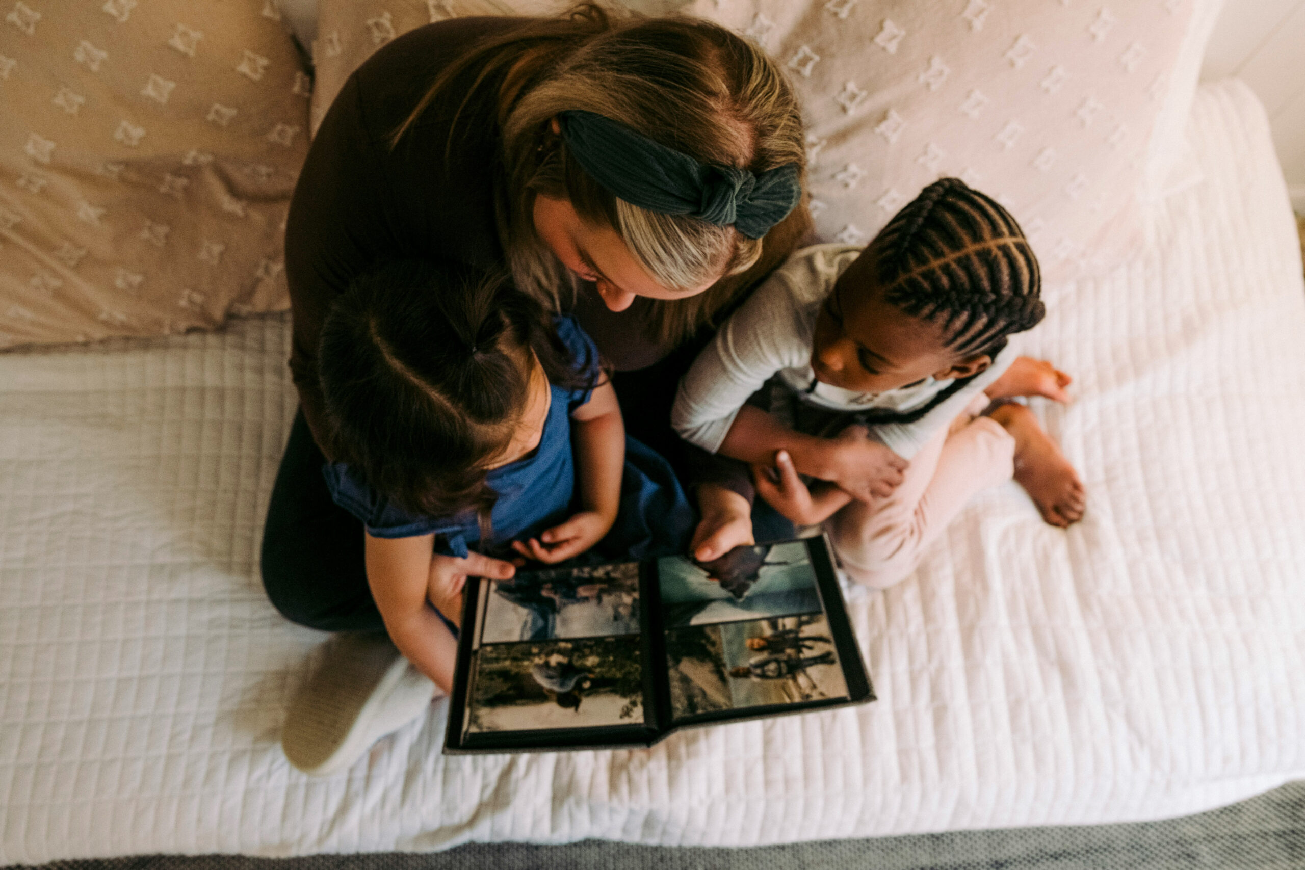 Mom reading a photo book with her two children on the bed