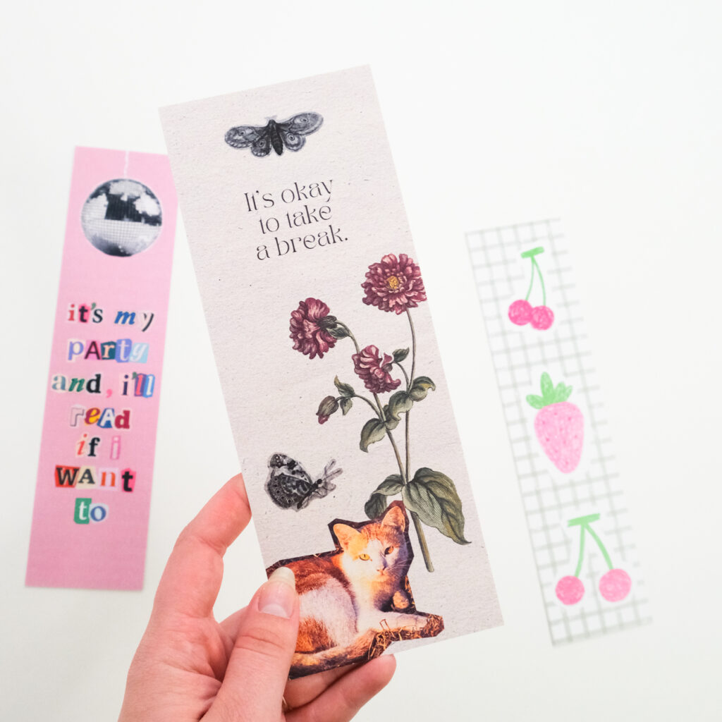 Hand holding three custom printed bookmarks with flowers, cherries, and a quote